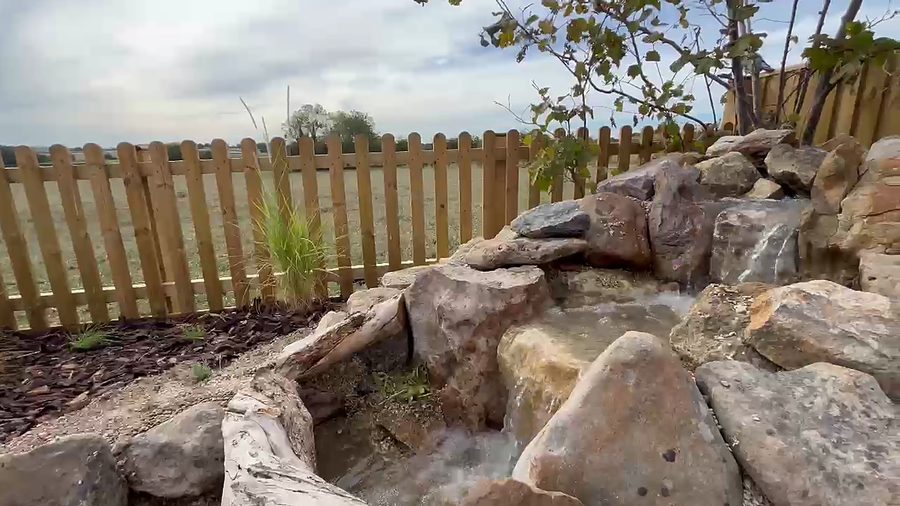 Water running down a cascade of large boulders into the new pond, beside a picket fence