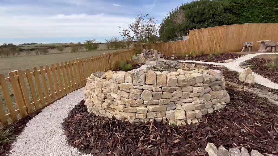 A circular drystone wall rising from a bed of bark mulch, ringed by a pale gravel path